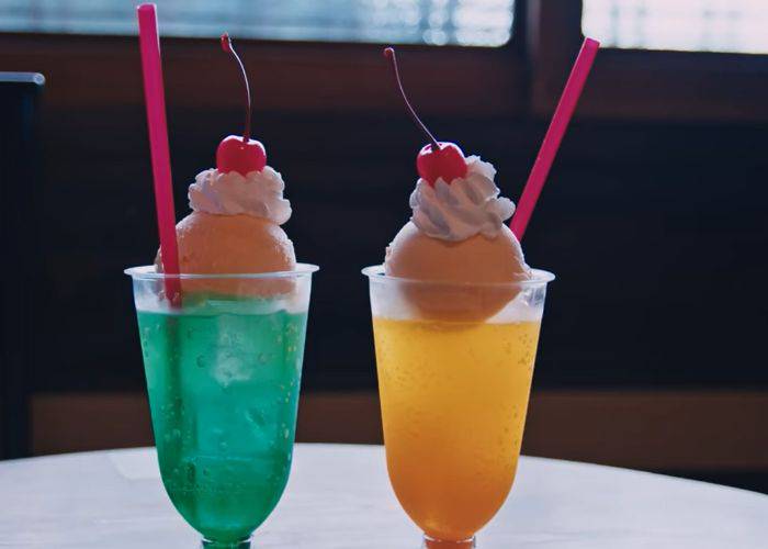 Melon and mango soda floats, each topped with a scoop of vanilla ice cream, whipped cream and cherries.